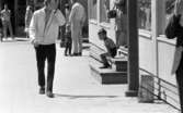 Kvar i stan 26 juli 1967

Ett antal människor befinner sig i centrala stan i Örebro. En ung man kommer gående. Han håller vänster hand framför ansiktet och är klädd vit jacka, ljus tröja, svarta byxor, vita strumpr och svarta skor. En liten pojke i fyraårsåldern klädd i svarta hängselshorts och randig T-tröja sitter på en liten trappa till höger. Ytterligare personer syns runtomkring.
