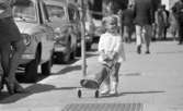 Kvar i stan 26 juli 1967

En liten flicka i tvåårsåldern drar på en rutig dockvagn där det sitter en docka. Hon är klädd i en långärmad, ljus blus, ljusa underbyxor, vita strumpor och vita skor. Hon går omkring i centrala stan i Örebro. I närheten av henne står en kvinna klädd i vit kofta, rutig kort kjol och lågklackade bruna skor. Flera vuxna människor syns i bakgrunden samt bilar som är parkerade längs med gatan