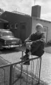 L. Person till USA, Oscaria 28 juni 1967

Närbild på en ung tonårspojke som sitter utanför sin familjs hus. Han är klädd i en mörk långärmad tröja, mörkrutiga byxor, svarta strumpor och svarta skor. En mörk bil står parkerad utanför huset.
