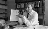 Lasarettet 14 juni 1967

En läkare sitter inne på sitt kontor vid sitt skrivbord. Han är klädd i vit läkarrock, vit skjorta och mörk slips. Bokhyllor och böcker syns i bakgrunden. Han demonstrerar ett diagram på ett papper.