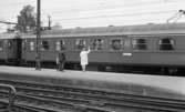 Frövi 2 juni 1967

På Frövi järnvägsstation står en kvinna i vit kappa, vita skor och som har en ljus handväska på vänster arm tillsammans med en man i ljus kostym och ett barn i tioårsåldern i ljus jacka, mörka byxor och ljus toppluva. De står på perrongen med ryggarna mot kameran och vinkar av passagerare som sitter inne i ett tåg framför dem.