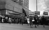 Första maj demonstration 2 maj 1967

Tre kvinnor går i förgrunden i ett första-majtåg utanför varuhuset Krämaren i Örebro. De är klädda i kappor och skor. Två av dem har hattar på huvudena. De bär skyltar med texten: 