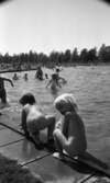 Grybe golf, Gustavsvik 17 juni 1967

Två små nakna barn sitter på huk i förgrunden med ryggarna mot kameran på utomhusbadet i Gustavsvik. I bakgrunden syns människor i alla åldrar som badar i bassängen. Många kvinnor och flickor badar i baddräkter och många män och pojkar badar i badbyxor.