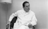 Göthman, Handikappfest,  18 maj 1967

En läkare klädd i vit läkarrock och vit skjorta sitter i en fåtölj. Bredvid honom står en golvlampa.