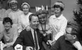 Luciafirandet 13 december 1966

En Lucia står tillsammans med ett antal tärnor vid ett bord i en skolmatsal. Lucian är klädd i vitt linne och har en Lucia- krona med ljus på huvudet. Runt halsen har hon ett halsband i form av ett hjärta med texten 