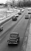 Länsläkaren, Trafiken 24 december 1966

Ett antal bilar, en lastbil och en bil med husvagn kör på en gata. Det ligger snö på marken. Hus syns i bakgrunden.