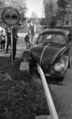 Dödsolycka i Almby 10 oktober 1967

En bil har krockat in i ett räcke och står mitt i vägen i Almby. En vägskylt syns vid gräsplätten och räcket som befinner sig mitt i gatan. En folksamling bestående av barn och vuxna män står i bakgrunden och betraktar förödelsen. En polisman står vid bilen.