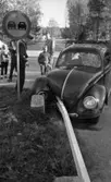 Dödsolycka i Almby 10 oktober 1967

En bil har krockat in i ett räcke och står mitt i vägen i Almby. En vägskylt syns vid gräsplätten och räcket som befinner sig mitt i gatan. En folksamling bestående av barn och vuxna män står i bakgrunden och betraktar förödelsen. En polisman står vid bilen.