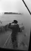 Vinöfärjan, Bandy, Hockey 6 december 1967

Vinöfärjans kapten poserar ombord på båten Han står med ryggen mot kameran ute på däck och tittar ut över sjön genom en kikare.