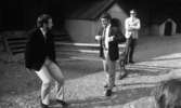 Wadköping (...?), 30 augusti 1968

Tre herrar som är skådespelare repeterar en föreställning utomhus i Wadköping. En av herrrarna sitter i förgrunden klädd i svart kavaj, vit skjorta, ljus slips, ljusa byxor, mörka strumpor och mörka skor. Nära honom står en herre som är klädd på samma sätt och därtill bär glasögon. Han heter Curt Skanebo. En lång bänk står bakom honom. Bakom denna står den tredje herren klädd i mörka solglasögon, vit kavaj, vit skjorta, mörk slips, ljusa byxor och mörka skor. Byggnader syns i bakgrunden.