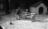 Wadköping (...?), 30 augusti 1968

Två herrar som är skådespelare repeterar en föreställning utomhus i Wadköping. En av herrarna som heter Curt Skanebo står i förgrunden med ryggen mot kameran framför en bänk och är klädd i svart kavaj, vit skjorta, ljus slips, ljusa byxor, mörka strumpor och mörka skor samt glasögon. På andra sidan bänken står en annan man på knä klädd i liknande kläder och färger.