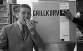 Korvätandet 30 augusti 1968

En man äter en grillkorv som han precis har köpt i en automat. Han är klädd i ljus kavaj, ljus skjorta och mönstrad slips.