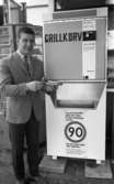Korvätandet 30 augusti 1968

En man står och håller i en grillkorv som han precis har köpt i en automat. Han är klädd i ljus kavaj, ljus skjorta, mönstrad slips, rutiga byxor, mörka strumpor och ljusa skor.