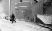Ytong 30 november 1967

Bild på en man som arbetar på Ytong. Han är klädd i mörk arbetsoverall med mörk keps på huvudet, mörka skor samt bär en väska i höger hand. Han har kommit ut ur en port ur en byggnad i bakgrunden.