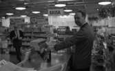 Hälsolivs, Vräktes 27 oktober 1967

En butikssäljare står vid kassan och håller en flaska i handen.