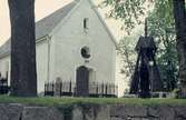 Almby kyrka utvändigt med klockstapel och kyrkogård.