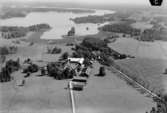 Flygfoto över Boskulla, bostadshus och ekonomibyggnader, sjöutsikt.