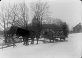 Två hästar spända för släde lastat med tunnor. En man.
Svennevads kyrka i bakgrunden.