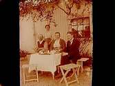 Ellen Larsson med sina föräldrar och herr Karlén runt kaffebordet i trädgården.