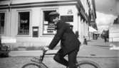 En man på cykeln. Affärsbyggnad i bakgrunden.
Schoultz Klädlager, Persil.
Korsningen Drottninggatan 24/Nygatan 15.
