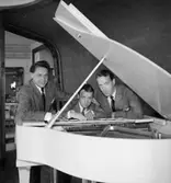 Glada Potpuriet, tre män vid pianot.
Rumsinteriör.