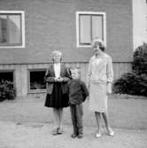 En kvinna och två barn.Bostadshus i bakgrunden.