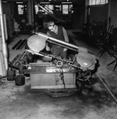 Verkstadsinteriör, en man vid järnsågen.
Gustafsson & Görtz