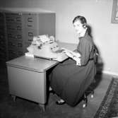 Kontorsinteriör, en kvinna vid skrivbordet.
Wigrell & Co, utställning på Idrottshuset.