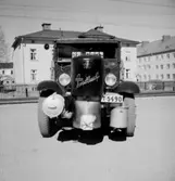 Lastbil med gasgenerator frammonterad.
Bostadshus i bakgrunden.