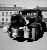 Lastbil med gasgenerator frammonterad.
Bostadshus i bakgrunden.