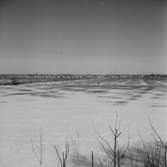 Vy. Åkermark i förgrunden, byggnader i bakgrunden.