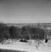 Vy. Åkermark i förgrunden, byggnader i bakgrunden.