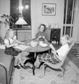 Rumsinteriör, en kvinna och två flickor vid bordet.
Jansson