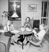 Rumsinteriör, en kvinna och två flickor vid bordet.
Jansson