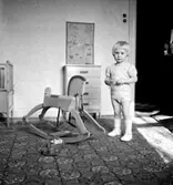 Rumsinteriör, en pojke med gunghäst. En kvinna.
Fru Larsson