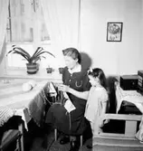 Rumsinteriör, stickning, en kvinna och en liten flicka.
Fru Hellkvist
Konsum