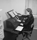 Konsum, kontorsinteriör, en kvinna.
Räknemaskin.