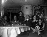 Rumsinteriör, familjegrupp sju personer vid bordet.
En del av familjen Pettersson, från vänster: Eva Sofia Pettersson (givarens farmor), ej namngiven kvinna, Ingrid Pettersson (givarens faster), Anders Johan Pettersson (givarens farfar), en pojke, Ester Pettersson och Kerstin Pettersson (givarens fastrar).