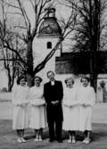 Konfirmander, fyra flickor och kyrkoherde Gabriel Carlsten.
Ekeby kyrka i bakgrunden.