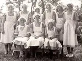 Skolklass. Gruppbild på skolköksflickor. Flickorna har ljusa förkläden och huvuddukar. Bilden är tagen utomhus.