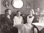 Diakonissan Valborg Kihlberg på hembesök. Hon sitter i en soffa tillsammans med två kvinnor.