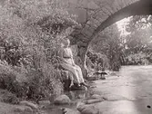 Dam sittande intill en bro över ett vattendrag. Tvååkers kanal?