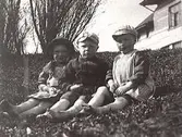 Tre barn fotograferade utomhus. I bakgrunden syns ett hus. Namnuppgifter saknas.