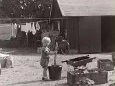 Ett litet barn leker ute på en gård där det bl a hänger tvätt. Det kan vara charkuterist Gustaf Petterssons uthus där slaktningen skedde i just den här porten.