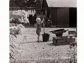 Barnlek. Litet barn leker ute på en gård där det bl a hänger tvätt. Kan vara charkuterist Gustaf Petterssons uthus där slaktning skedde i just den här porten. .