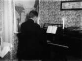Rumsinteriör, en man vid pianot.
Pianist på besök i Hagalund.