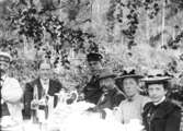 Grupp sex personer vid kaffebordet i trädgården.
Troligen år 1901.