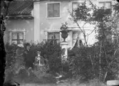 Familjegrupp fyra personer i trädgården.
Bostadshus i bakgrunden.