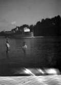 Badplats, två personer i vattnet, ångbåten Rättvik i bakgrunden.
Dalarna.
