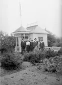 Örebro kolonien.
Stuga, grupp sju personer framför stugan.